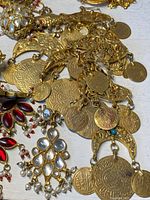 Photo showing a close-up of coin necklace and earrings with clear and red stones featuring intricate metalwork and small dangling pearls