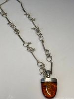 Full view of the silver chain necklace with decorative links and the amber pendant.