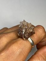 Close-up photo of a hand wearing the silver band ring set with a natural raw quartz geode cluster showing its crystalline textures and colors.