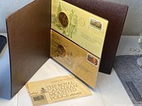 The open leather folder displaying two large silver medals and commemorative stamped envelopes.