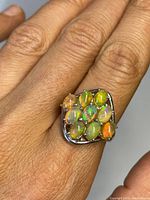 Close-up front view of the silver ring with nine opal stones showing vibrant color plays on a finger.