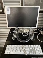 Front view of Apple Cinema HD Display monitor on clear acrylic stand with Apple wired keyboard in front