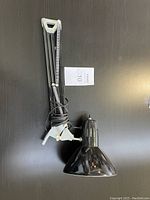 Black articulated arm lamp seen in full view showing adjustable arm and conical shade with power cord wrapped around base.