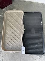 Image showing two boot mats side by side on concrete floor, one beige with lattice pattern, one black with grooves, both used condition.