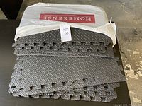 Stack of gray interlocking foam mats with diamond plate texture and some pieces cut, in HomeSense packaging bag.