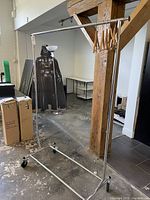 Overall view of the chrome garment rack with adjustable horizontal hanging bar and five wooden hangers included. The rack stands on four caster wheels and is in a used condition.