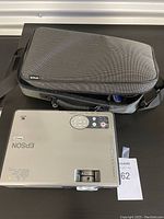 Epson projector with carrying case on a table, showing top control panel and brand name.