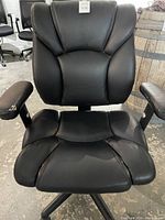 Front view of black faux leather office chair showing padded ergonomic design and wear on armrests and seat.