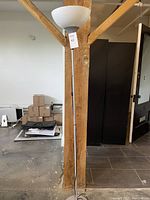 Floor lamp standing tall showing its height and design against a wooden post in an indoor setting.