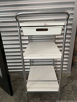 White Ikea storage cart on wheels with one drawer and three shelves framed in metal with chrome finish