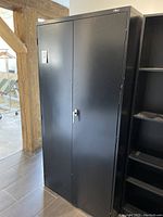 Front view of closed black metal storage cabinet with dual doors and latch handle.