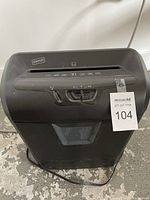 Front view of a small black Staples paper shredder with slot and control switches on the top and power cord on the bottom, showing overall condition and brand label.