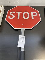 Front side of handheld stop sign showing red octagonal stop sign with white letters and attached handle with black grip on dark surface.