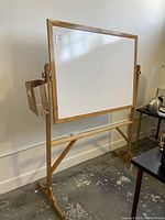 Side view of wooden framed, double-sided white board on freestanding wooden support with visible wood grain finish.