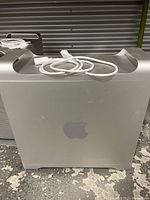 Side view of one aluminum tower showing smooth panel with Apple logo and bundled power cable on top
