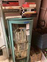 Books on top of and inside a blue-green glass front cabinet, showing a variety of books from political, historical, and fiction genres.
