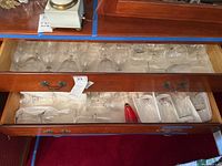 View of upper drawer containing mostly various clear stemware including the wine glass marked Seneca and hand-painted champagne flutes with red floral designs