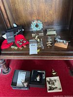 Overview of various lot items including jewelry inside red velvet pouches, metal boxes, silverplate bird figurines, a metal wreath decoration, and other small decorative items on wooden surface.