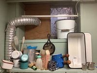 View of shelf with various enamelware items including bucket, metal cups, fondue pots, bottle caps, and small enamel pots and utensils