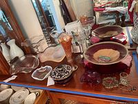 Overall view of glass serving ware collection including bowls, carnival glass vase, lidded dish, and other decorative glass items on a wooden table.