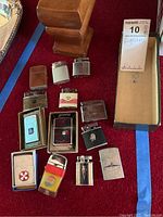 13 assorted flip-top and push-button lighters laid out on red felt