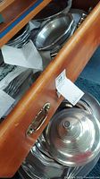 Drawers filled with stacked pewter trays, bowls, with some covered serving dishes visible.