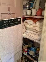 Photo showing Laura Ashley white reversible bath rugs hanging on the door with label visible, shelves with folded towels, and various medical and bath supplies.