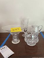 Photo showing Steuben crystal bowl with yellow size tag and three Waterford crystal pieces behind it on a wooden surface.