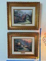 Two framed and matted Thomas Kincaid prints hanging on a wall, showing the full front view of both artworks in gold ornate frames.