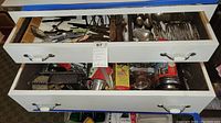 Two open drawers showing assorted cutlery, utensils, graters, scoops, and measuring cups, metal and plastic handled, visibly worn