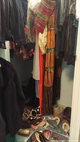 Photo showing assorted clothing hung on hangers including jackets, blouses, dresses, with shoe stretchers and shoes on the floor.