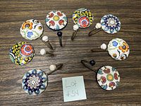Set of 10 ceramic wall hooks arranged in a circle showing varied colorful floral and geometric pattern tops with white and black ceramic end tips on metal hooks.
