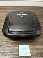 Closed top view of the black George Foreman grill showing red and green indicator lights and some usage marks on the lid.