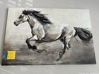Close-up photo of the rectangular canvas painting of a running horse in neutral tones.