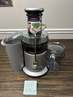 Front view of Breville juicer with juice pitcher and pulp container showing the feed tube with documentary sticker