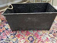 Side view of rectangular black metal trough basket showing weathered finish and rope handle.