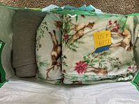 Photos showing 5 blankets folded and stacked inside a bag: 1 solid gray, 4 with green background and deer/flower pattern.