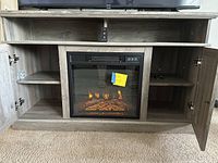 Front view of TV stand showing open doors, interior shelves and fireplace lit