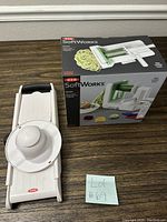 Veggie slicer next to the boxed spiralizer on a wooden table with a lot number tag.