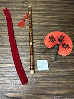 Photo showing the bamboo flute, the red velvet carrying case, and the decorative folding fan placed on a wooden surface with a lot number note.