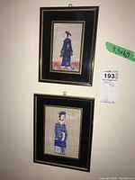 Both framed prints shown hanging on wall, black frames with gold trim and images of Asian figures in traditional clothing.