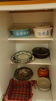Inside cabinet shelf with Pyrex and other ceramic dishes, plates, bowls, and metal bowl