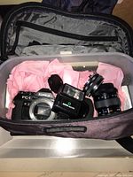 Top-view inside carrying bag showing Konica FC-1 body, flash unit, and extra lens on pink lining