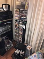 CD shelving tower with multiple jewel case CDs, loose CDs at base, black fabric CD carrying case to left.