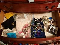 Drawer of assorted jewelry including necklaces, bracelets, earrings, jewelry bags, and a small purse