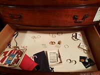 Wide shot of drawer showing manicure set, various earrings, necklace, sheet music, and small pouch