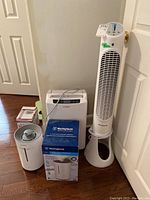 Photo showing all three items: Honeywell QuietSet tower fan, Westinghouse dehumidifier with box, and Waykar dehumidifier clustered near a door.