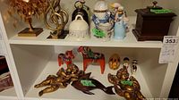 Shelf displaying two gold cherub wall hangings, two hand-painted red wooden horses, a decorated egg-shaped piece, small cultural figurines, blue duck figurine, white bell, wooden box, and wood music note bell.