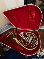 Top-down view of French horn seated in open case showing red plush interior
