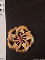 Front view of brooch showing swirl design, hearts and central pink stones